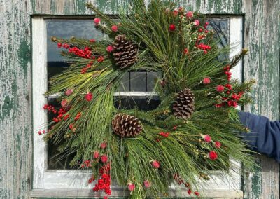 Christmas Wreath with red berries and pinecones in front of an old barn door
