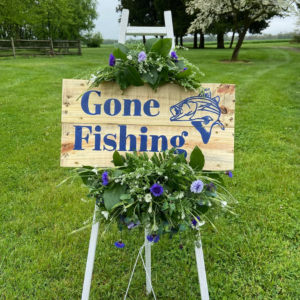 Funeral easel with flower arrangement and fishing sign