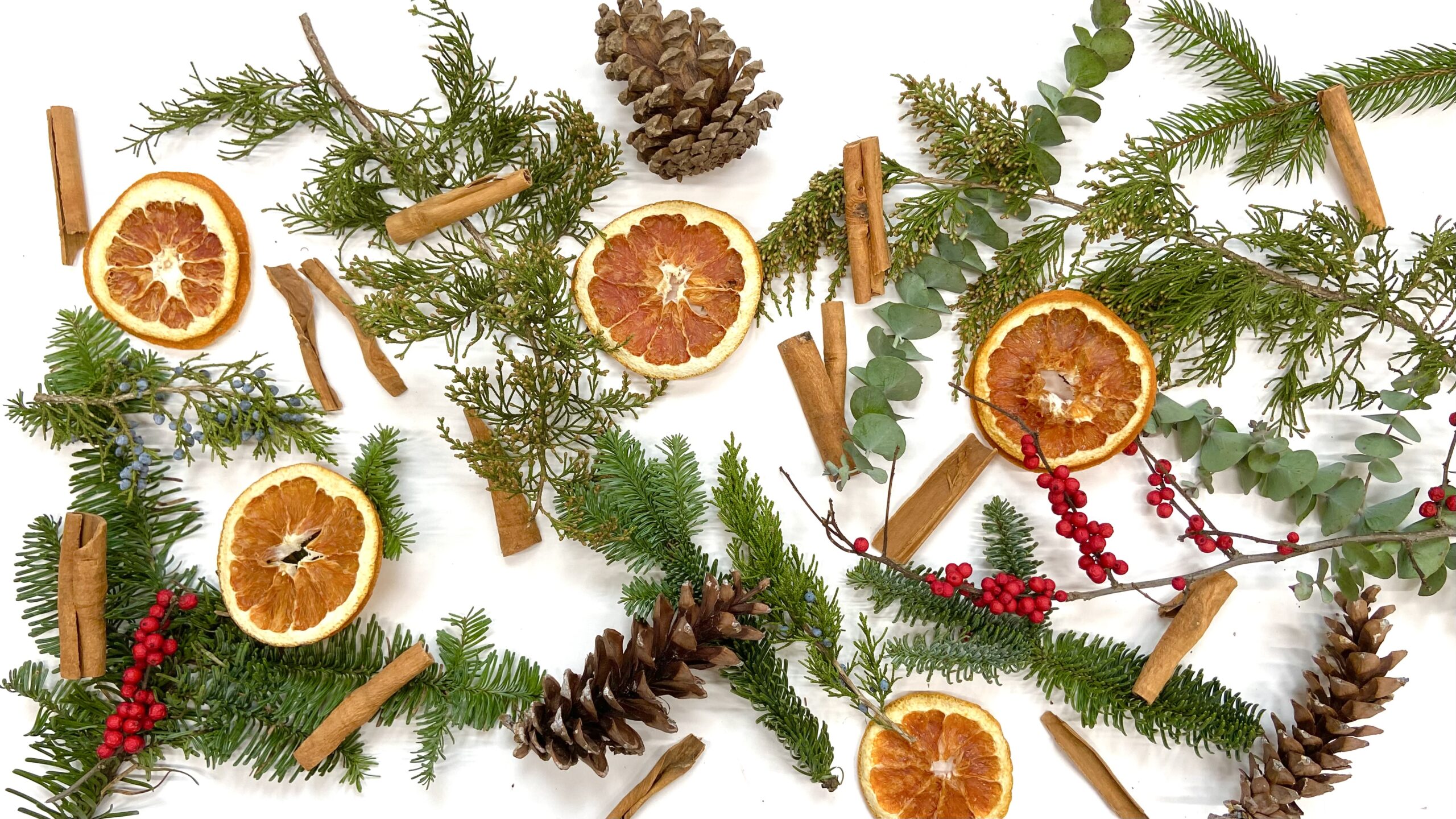 Scattered orange slices, winter greens, cinnamon sticks, pine cones, red berries