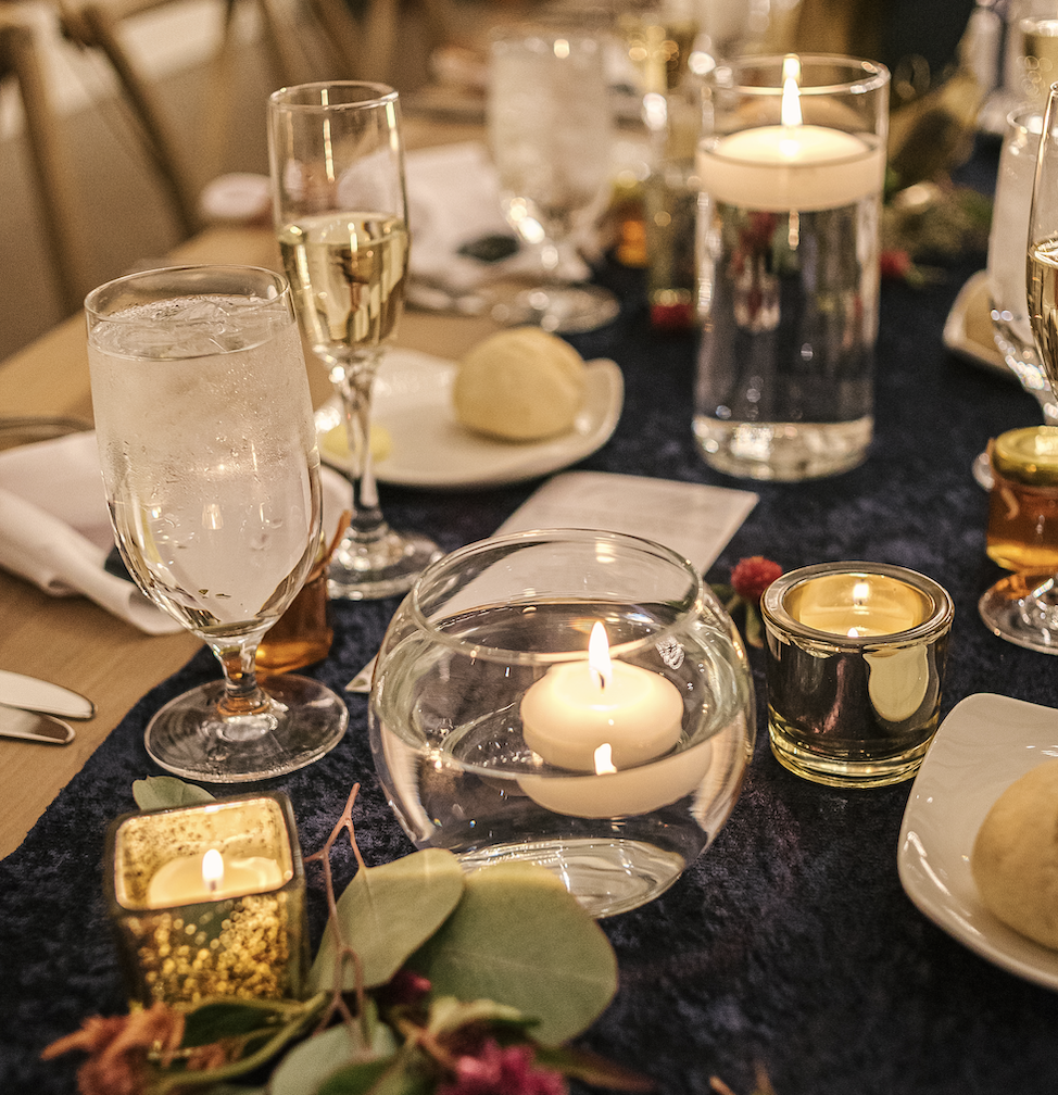 Farm table with candles, glass votives, gold votives, greenery, and floating candles.