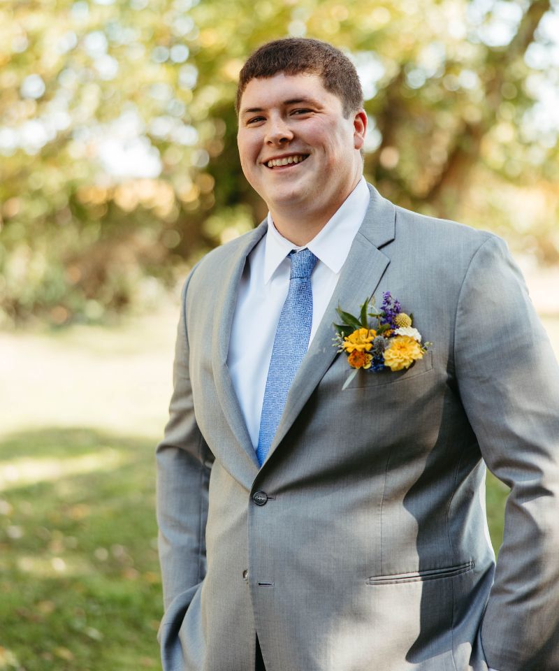 groom standing with gold and blue flowers in pocket square