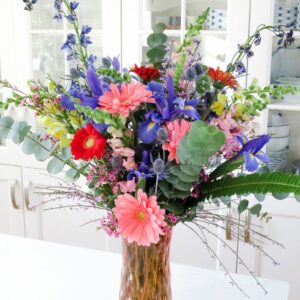 Large and full colorful flower arrangement in a pink glass vase on a white countertop