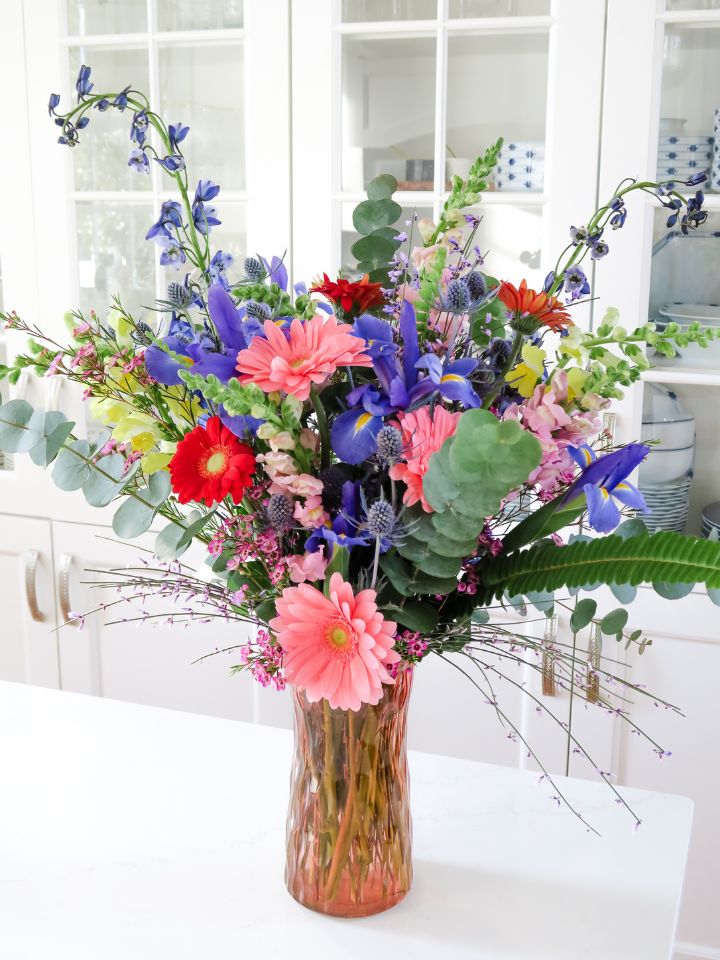 Large and full colorful flower arrangement in a pink glass vase on a white countertop