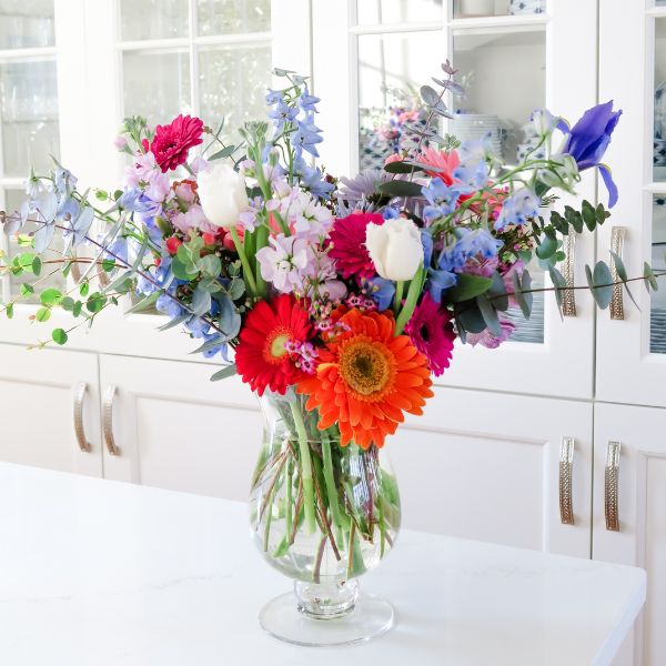 Colorful Valentines flower arrangement in clear glass vase sitting on white countertop