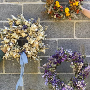 Three dried wreaths against a cement block wall.