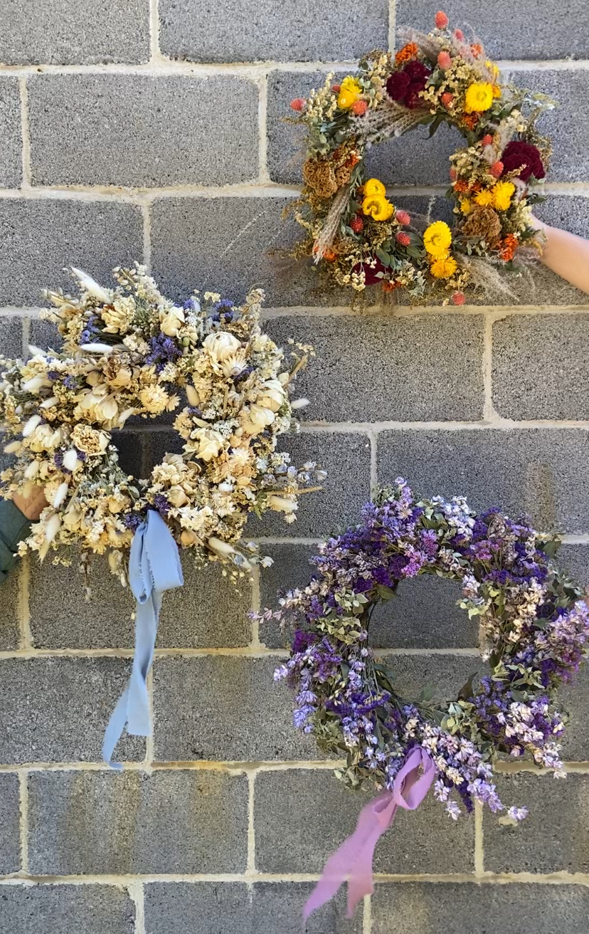 Three dried wreaths against a cement block wall.