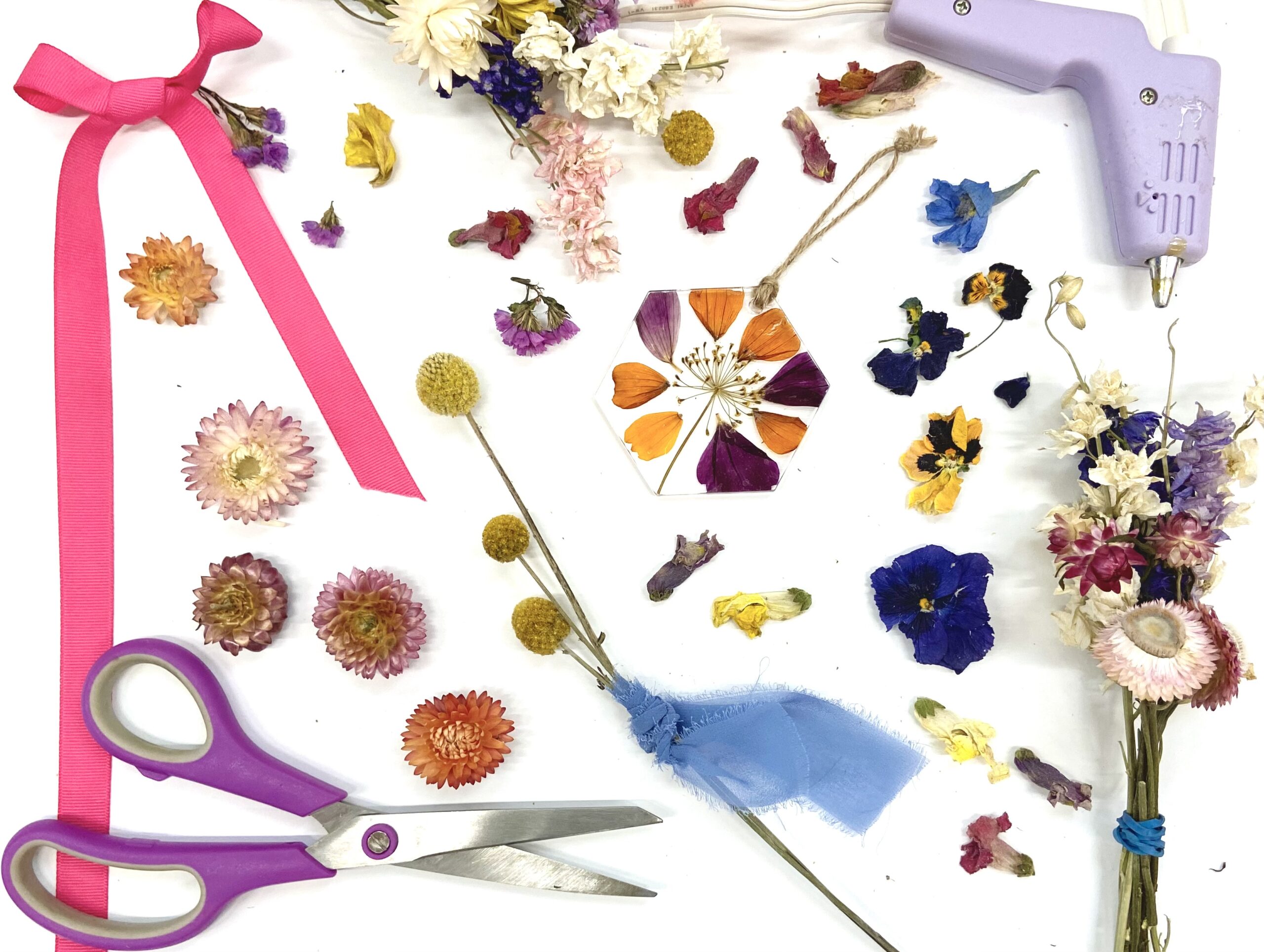 Flat lay on white background of scissors, glue gun, ribbon, and dried flowers for crafting