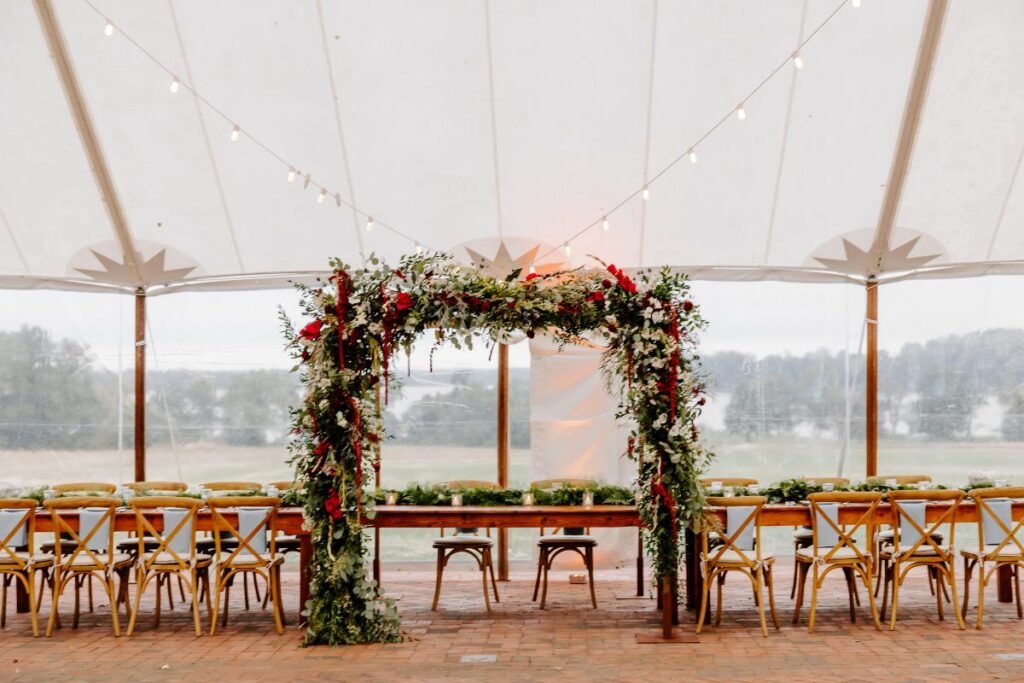 Floral chuppah underneath a sailcloth tent with head table on brick patio at Brittland Manor.