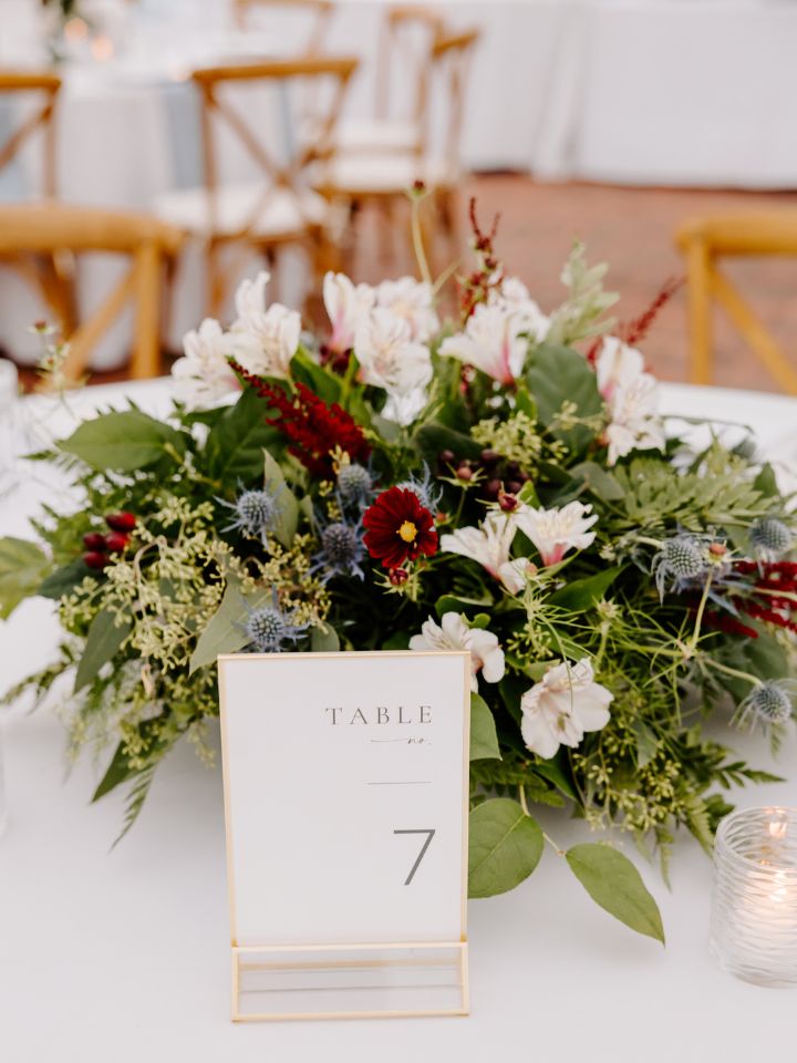 Low round floral arrangement in maroon, white, and dusty blue at a wedding reception.