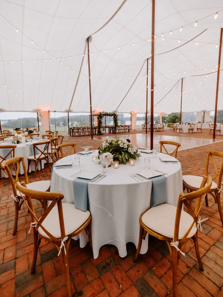 View of under the sailcloth tent on a brick patio with wedding reception tables.