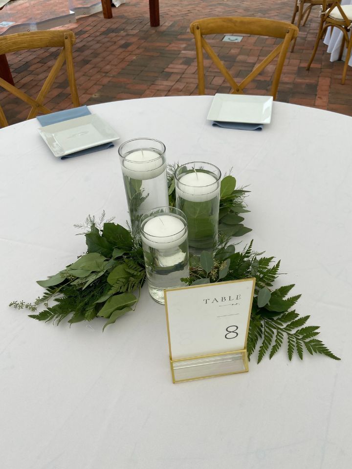 Trio of floating candles in varied height glass cylinders with mixed greenery.