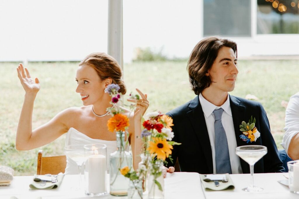 Bride and Groom sit at the head table, with a white tablecloth and colorful bud vases with summer flowers.