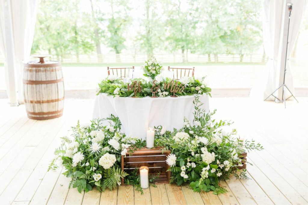 Sweetheart table with white and green wedding flowers and wooden crates in front.