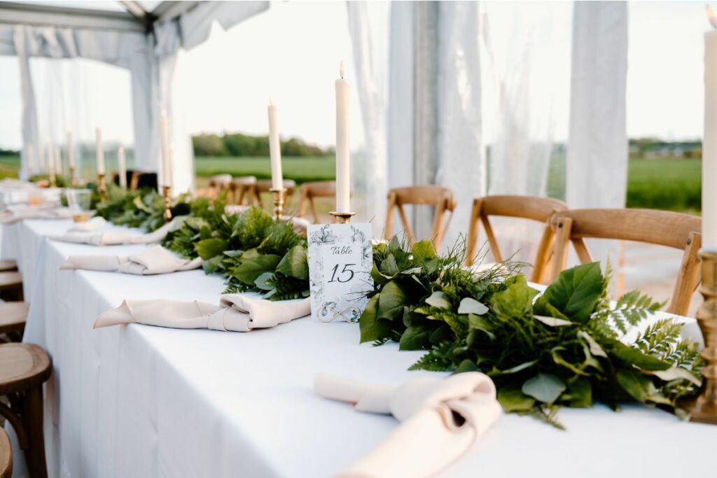 White tablecloths on long rectangular reception tables with taper candles and greenery table garland.