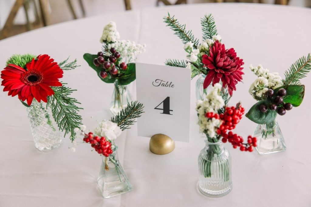White tablecloth set with a table number and bud vases with Christmas flowers.