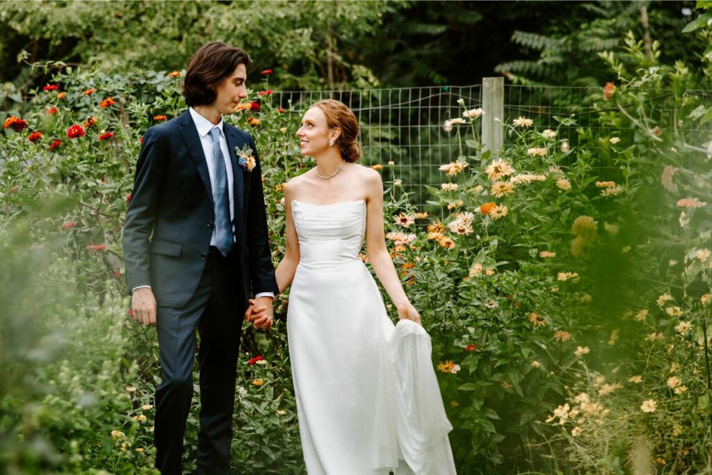 Bride and groom pose looking at each other in a lush green flower garden.