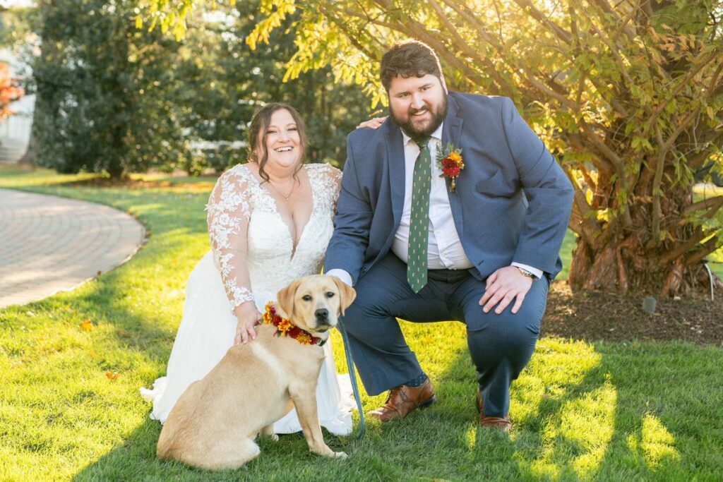 Bride and Groom kneel with their dog in a floral collar.