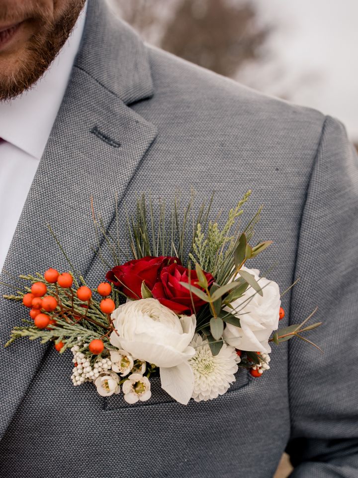 Close up of a grey suit with a floral pocket square style boutonniere for a wedding, in Christmas colors.