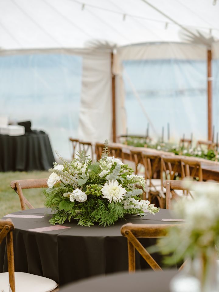 Wedding reception sailcloth tent with black round tablecloths and wood harvest tables, with white and green wedding flowers.