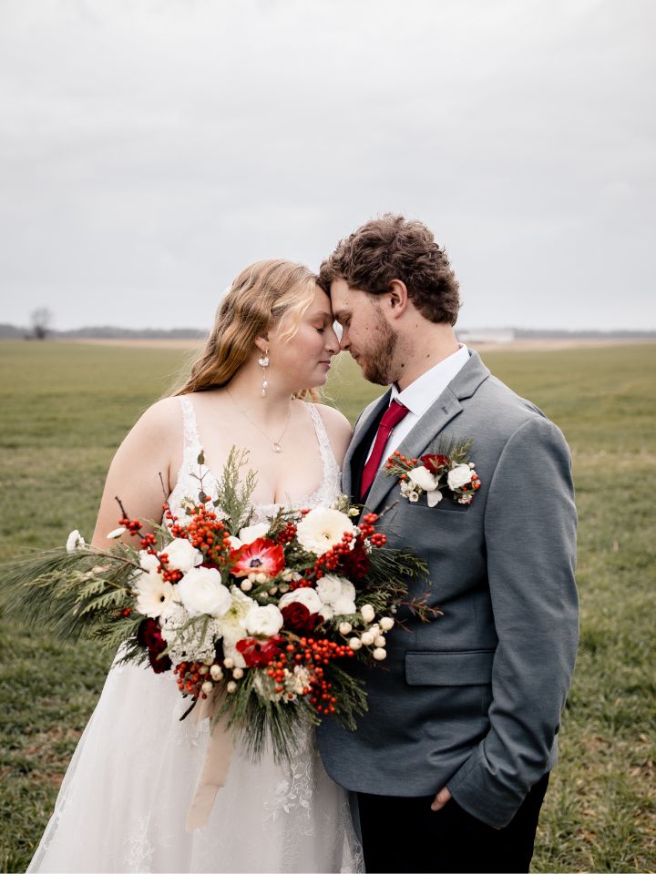 Bride and Groom pose together near a field, holding Christmas wedding flowers.