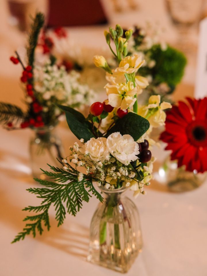 Bud vase with Christmas florals on a white tablecloth.