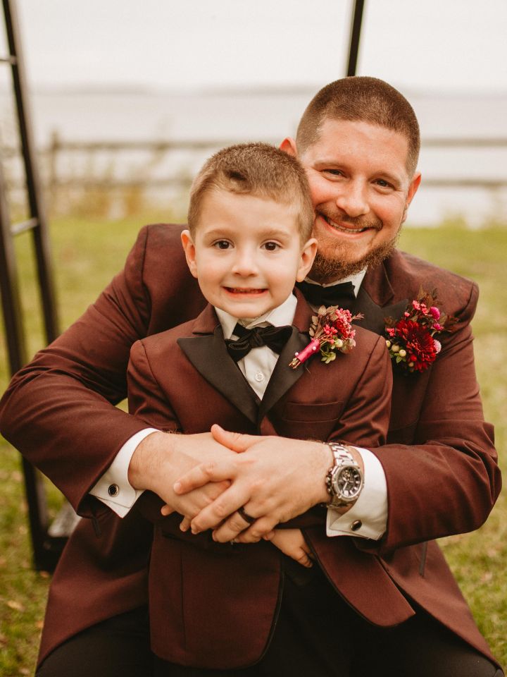 Groom and son wear maroon suits with dark flower boutonnieres.
