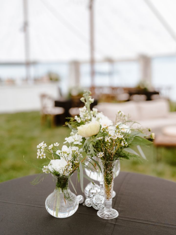 Scattered bud vases on a black table cloth with white flowers and disco balls.