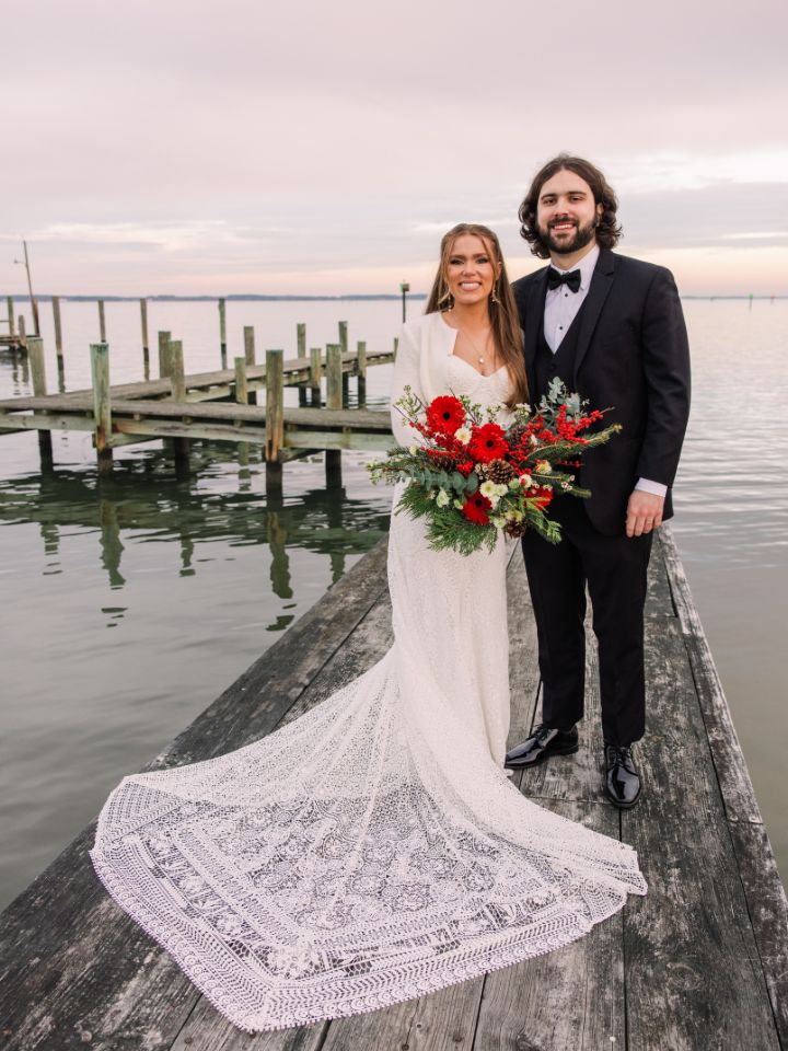 Bride and Groom stand on a dock at sunset with Christmas Wedding Flowers