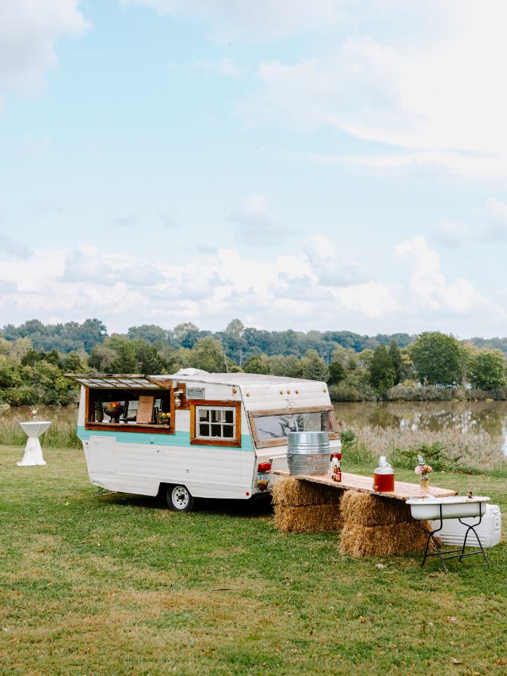 Vintage camper set up as a bar at a wedding near a grassy field.