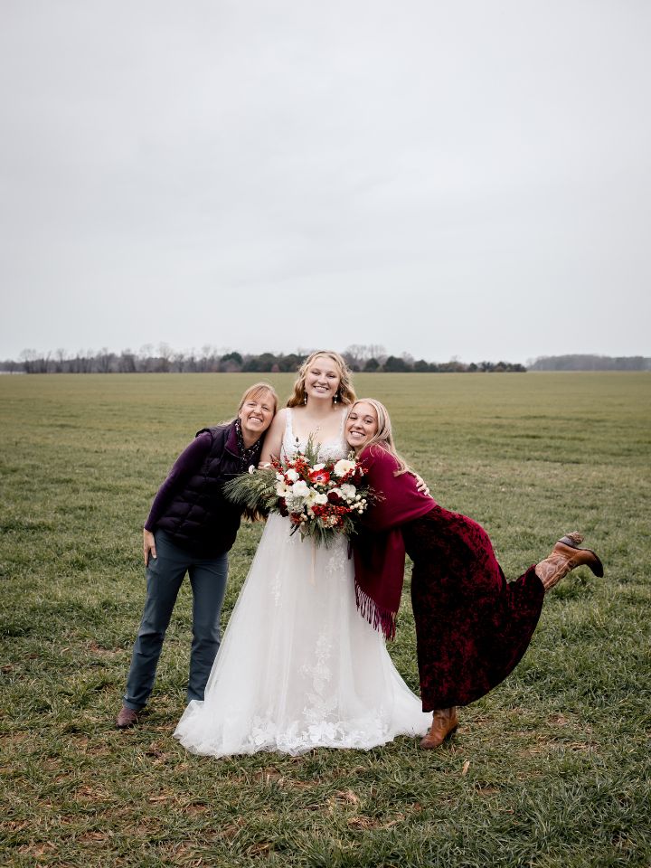 Two women stand on either side of the bride, who is holding her Christmas wedding flowers, all smiling.