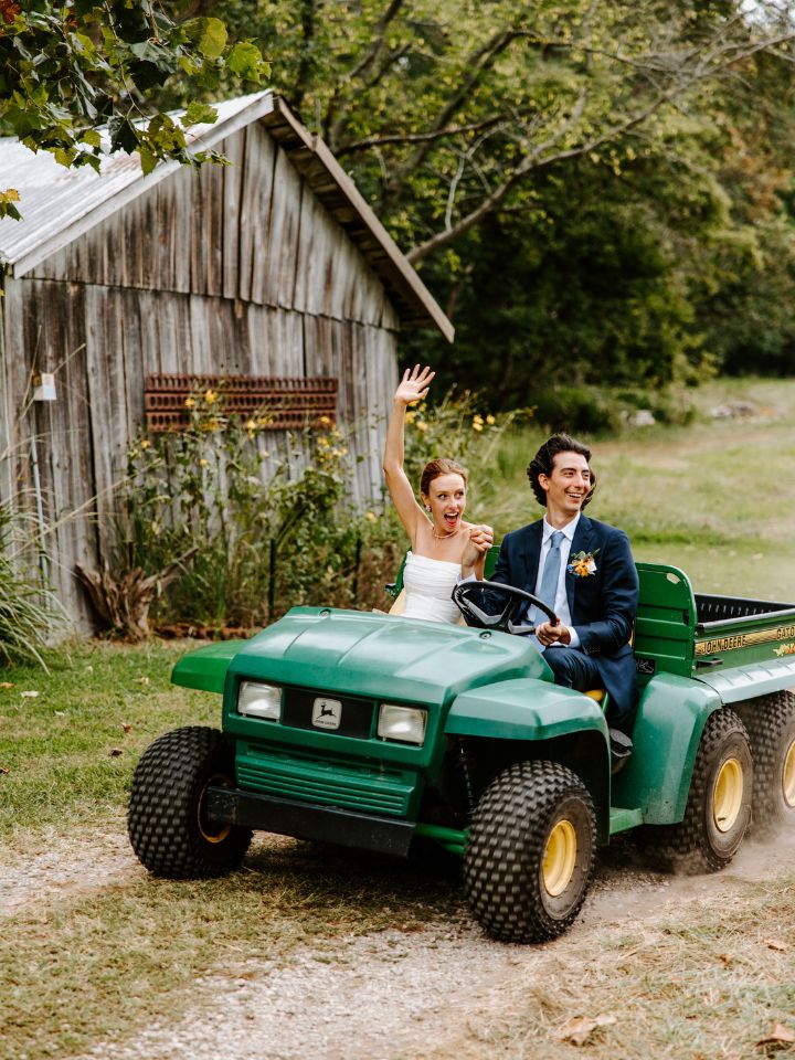 Bride and Groom ride in a green gator past an old wood outbuilding after their wedding ceremony.
