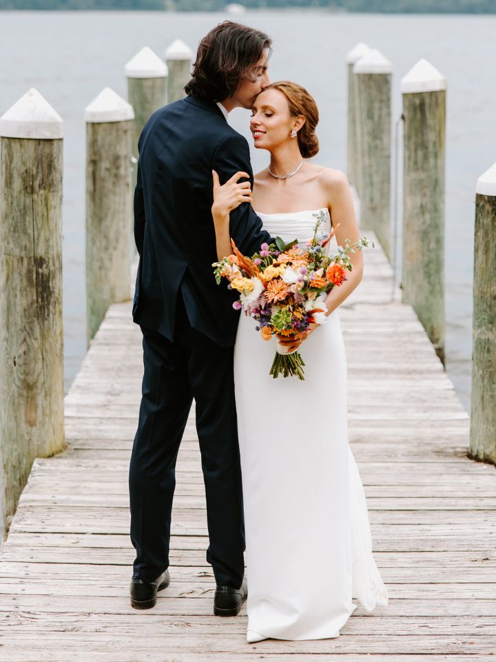 Bride and Groom pose on a dock, holding a bright summer wildflower wedding bouquet.