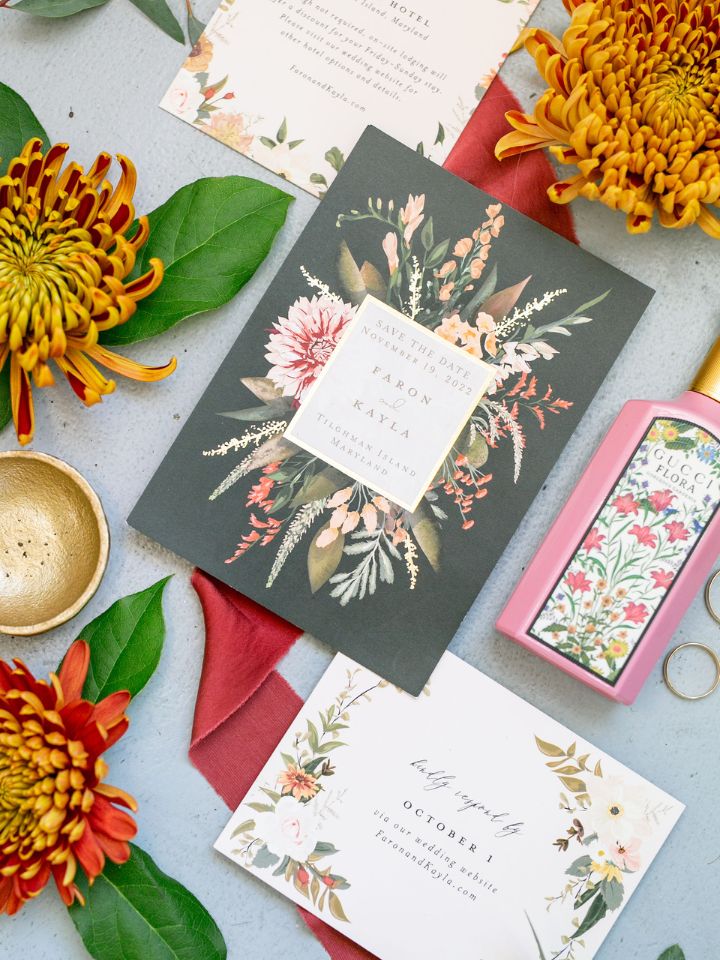Flat lay photo on light blue backdrop with wedding invitation, florals, and perfume.