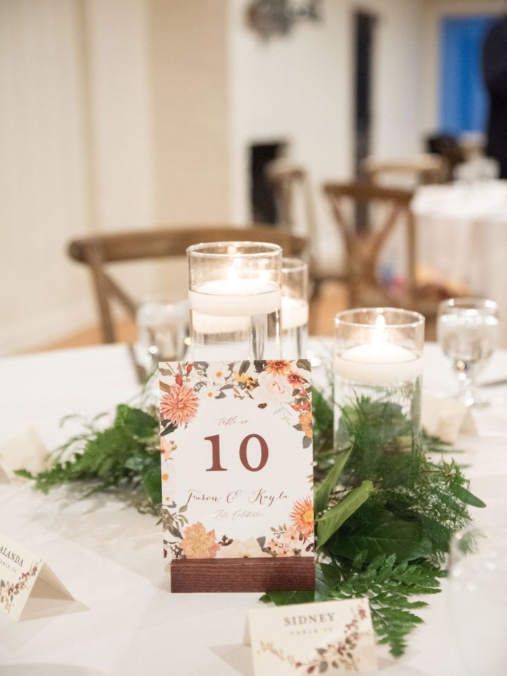 Reception table has a white table linen with table number, floating candle in glass cylinder trio, and greenery.