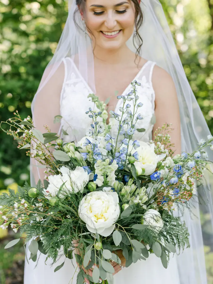 Bride with veil looking down at her blue, white, and green bouquet of florals