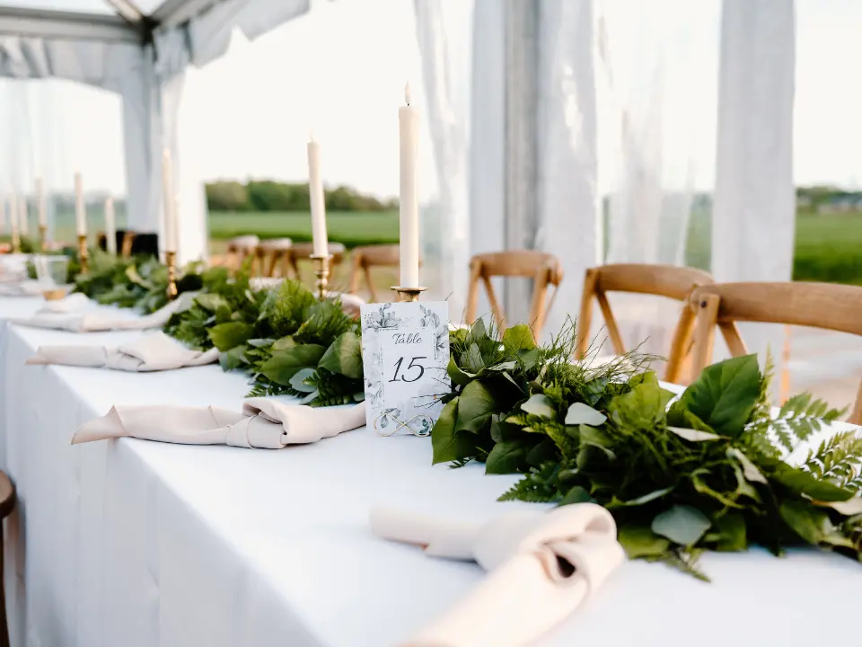 Rectangle table s lined up together with a white linen and a centerpiece of greenery