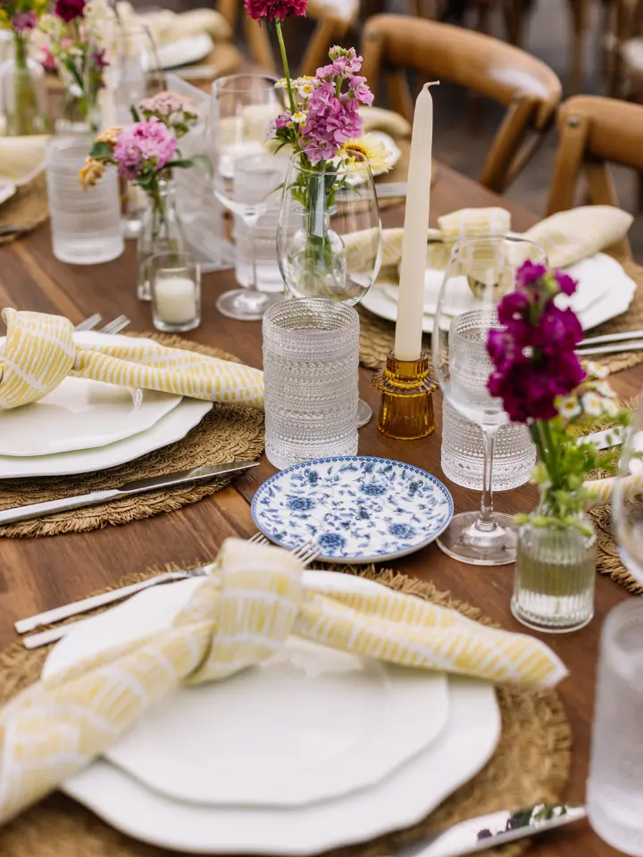 Up close table setting with yellow napkin knotted on top of white plate with bud vase florals