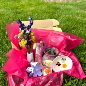 Mailer box is opened and sitting in grass, with hot pink tissue paper and floral membership subscription items shown inside.