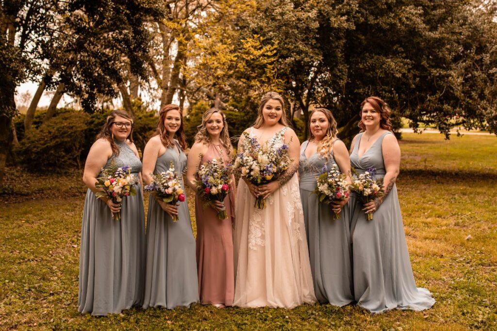 Bride and bridesmaids hold their spring wedding bouquets and smile towards the camera.