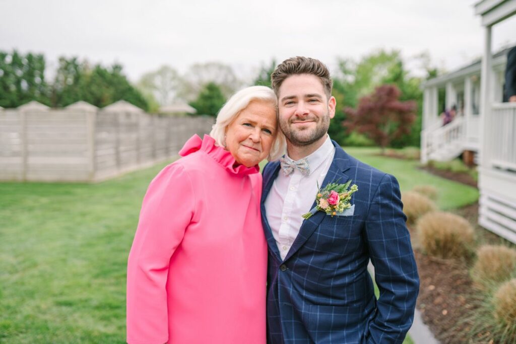 Groom and his mother smile at the camera at a wedding,