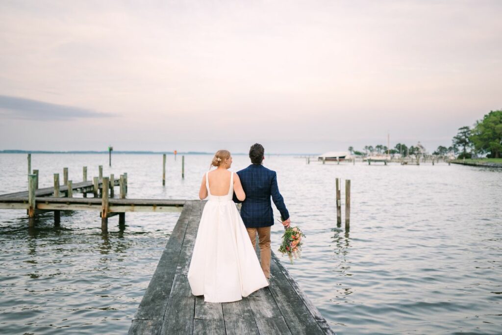 A bride and groom walk on a dock during sunset at their wedding.