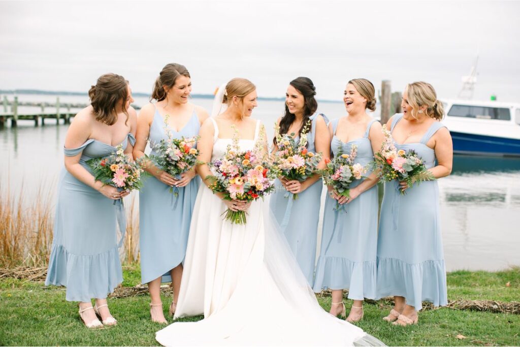 Bride and her bridesmaids hold their spring bouquets and smile at each other.