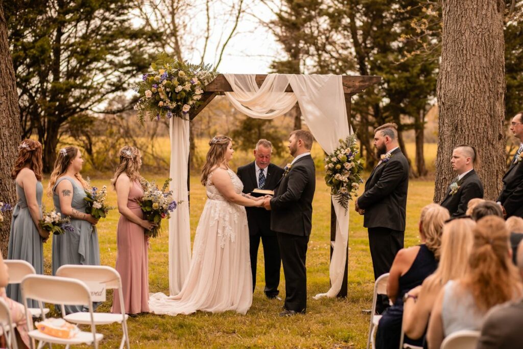Bride and groom stand at ceremony arch with spring floral and fabric draping.