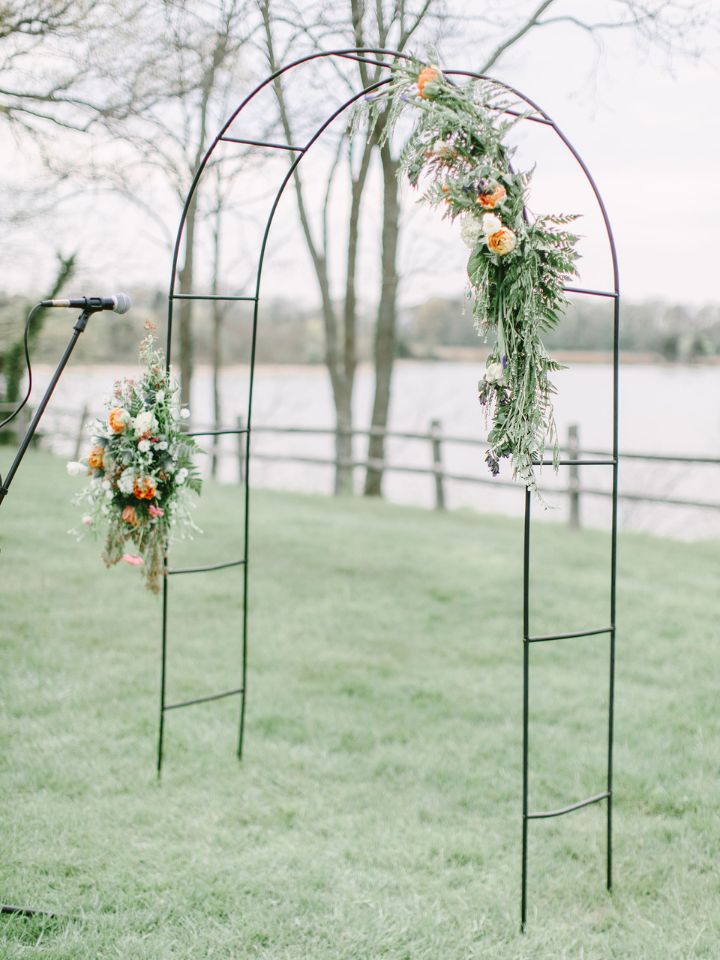 Black metal rounded wedding ceremony arch in an outdoor setting with light floral accents.