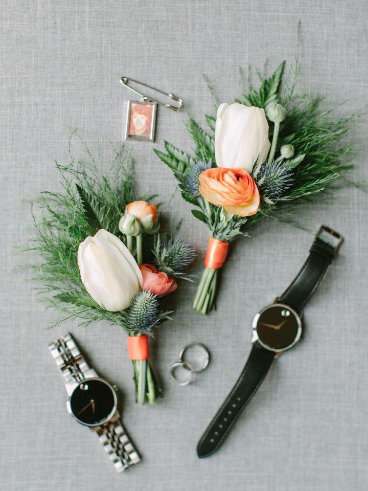 Flat lay photo of two boutonnieres, rings, and watches.