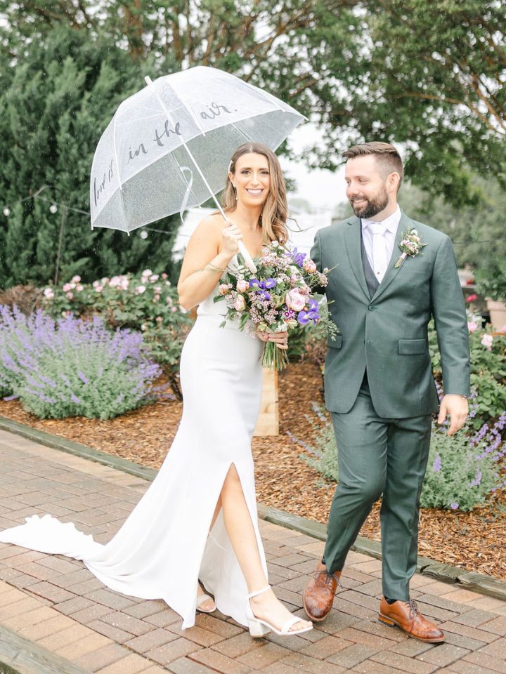 Bride and Groom walk through garden under an umbrella.