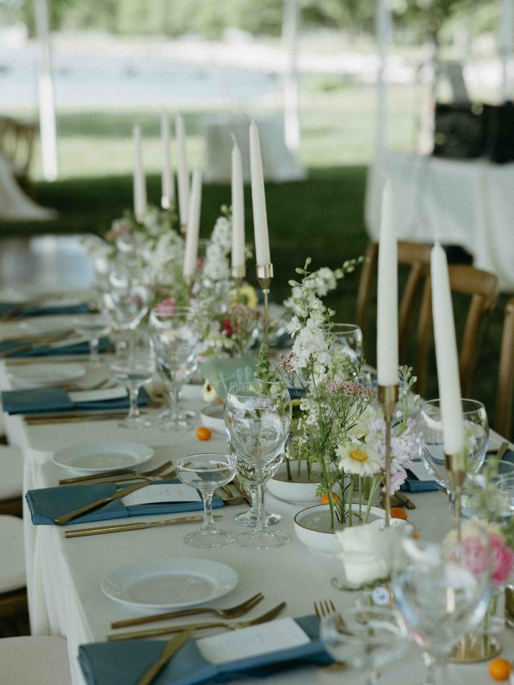 Wedding reception table with white tablecloth, blue napkins, gold candlesticks, and floral frog dishes.