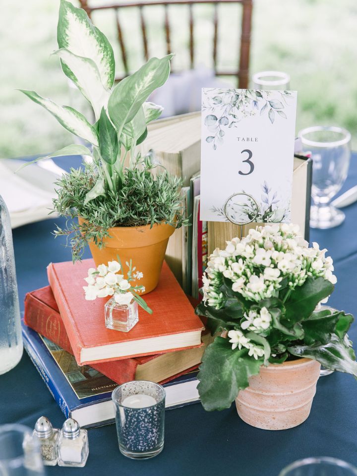 Potted plants and bud vases sit on vintage books at a wedding reception table.