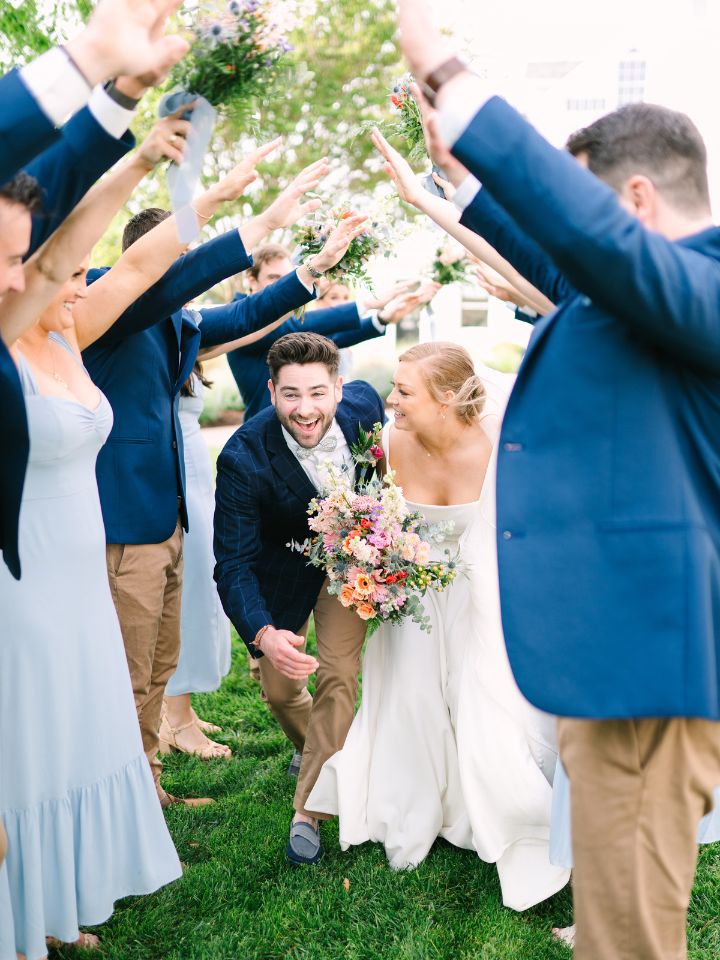 Bride and Groom go through a tunnel of their wedding party with arms raised.