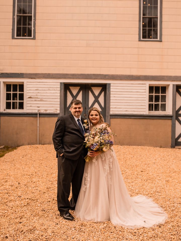 Couple stands in front of barn backdrop at wedding.